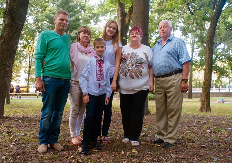 Family if four (father, mother, daughter, son, grandfather and grandmother) in a lush green park setting
